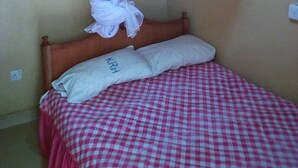 A bedroom with a bed covered in a red and white checkered bedspread, a white pillow with 'KRH' embroidered on it, and a wooden headboard. - Kwiremia Hotel (Embu)