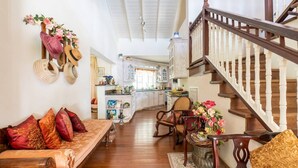Amplia sala de estar con una escalera de madera, una cocina al fondo y un comedor con mesa y sillas.