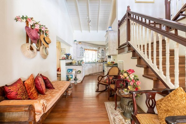 A spacious living room with a wooden staircase, a kitchen in the background, and a dining area with a table and chairs.