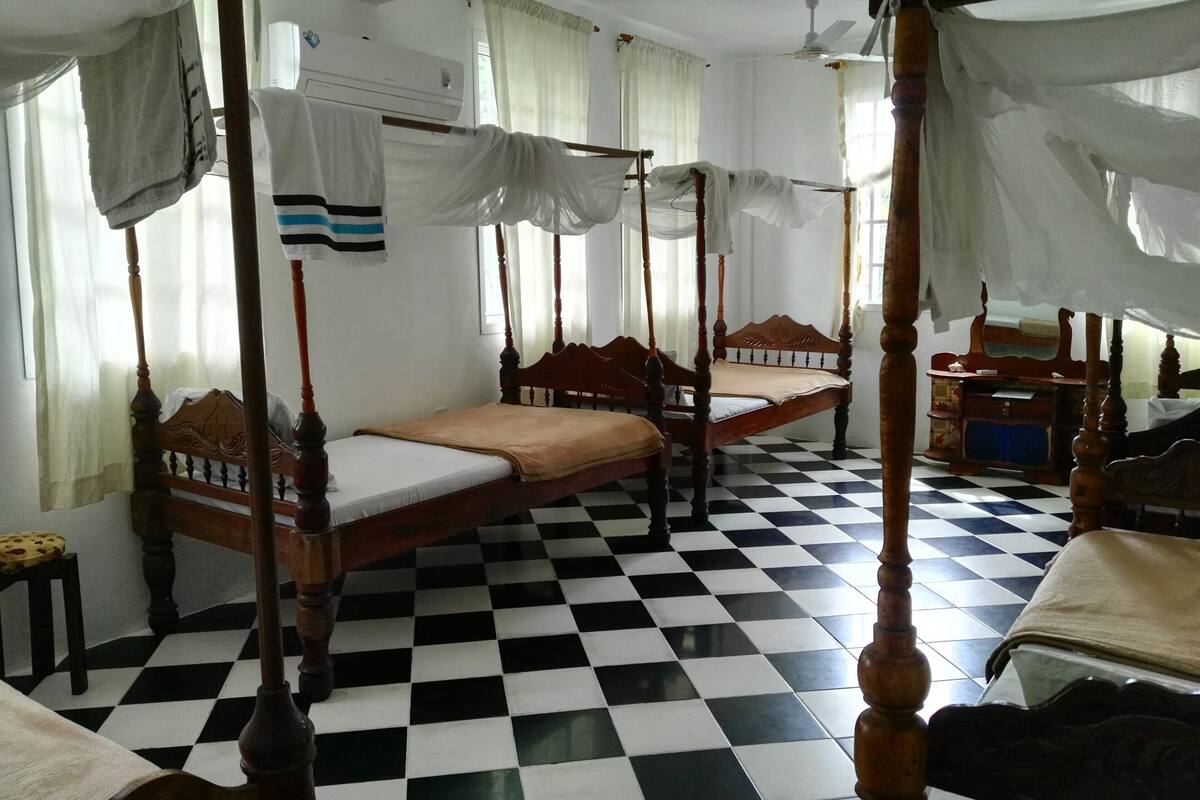 A room with four wooden four-poster beds, a checkered floor, and a window with curtains.