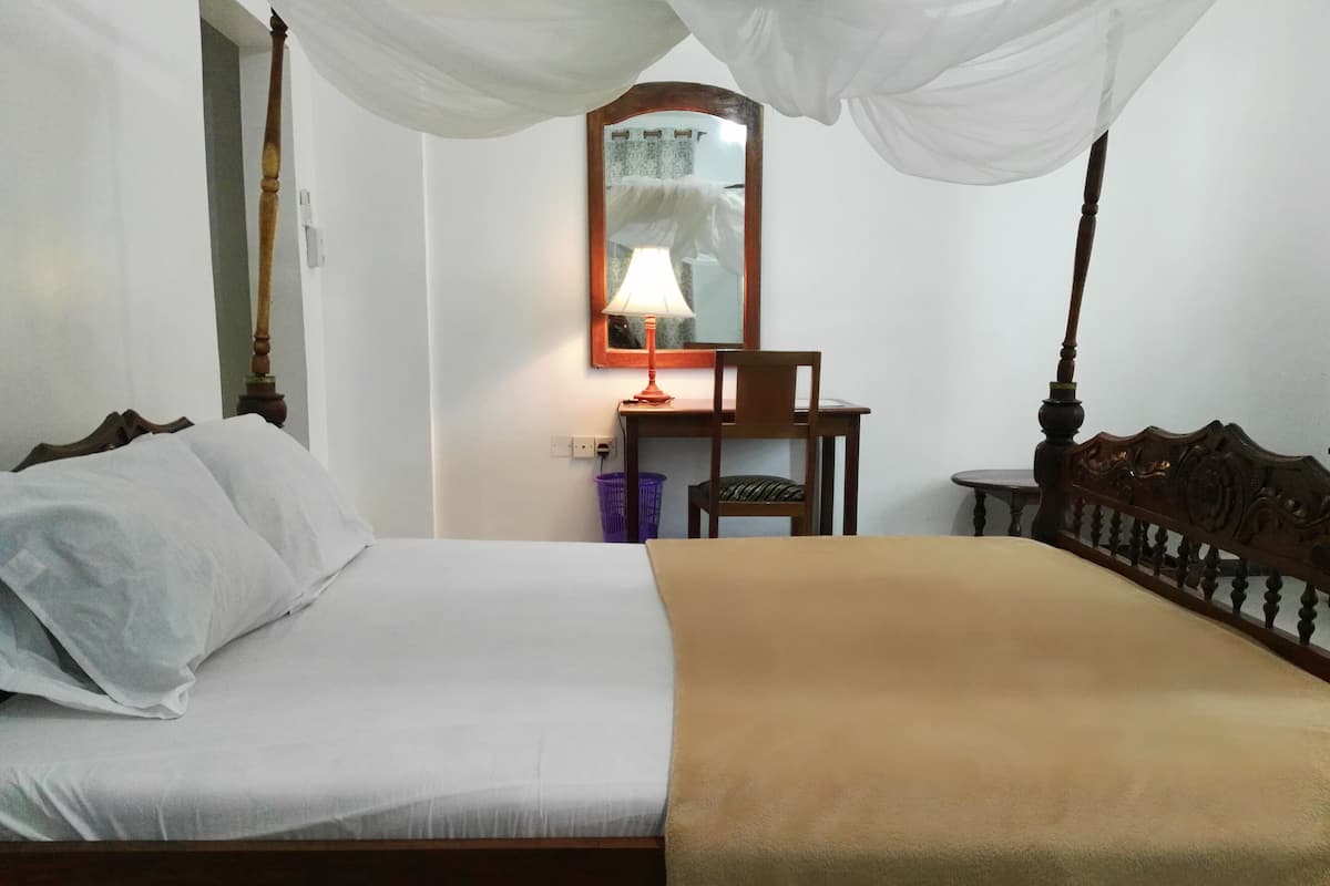 A hotel room with a bed, a chair, a small table, and a lamp.