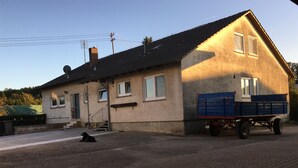 Et toetagers hus med skråtag, en blå lastbil foran og en hund, der ligger på jorden.