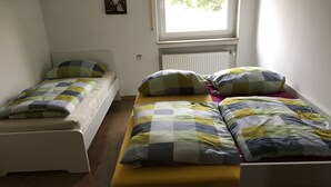 Et værelse med to senge, en med gul madras og en med hvid madras. Der er et vindue med udsigt til grøn vegetation udenfor.