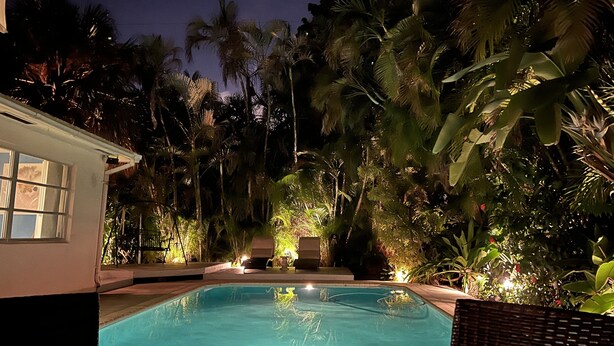 Une piscine entourée d’une végétation tropicale luxuriante et un bâtiment doté d’une fenêtre bien visible.