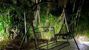 Une balançoire installée dans un jardin tropical, avec une structure en métal et un siège en bois, entourée d’une végétation luxuriante.