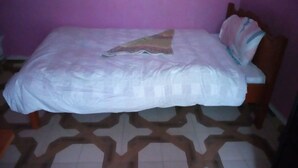 Una cama individual con una colcha estampada y una almohada decorativa en una habitación con pared morada y diseño geométrico en el suelo.