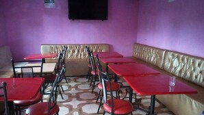 Interior de restaurante con mesas y sillas rojas, un banco acolchado color beige y piso estampado.