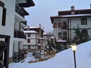 Lumipeitteinen asuinkatu, jossa on useita kerroksia sisältäviä rakennuksia, parvekkeita ja katulamppu.