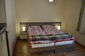 Makuuhuoneessa on puinen sängynpääty, yöpöytä lampun kanssa ja sänky, jossa on punavalkoinen kuviollinen peitto.