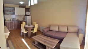 A modern living room with a sofa, a dining table with chairs, a kitchen area with cabinets and appliances, and a wooden floor. - Apartment for rent in the Rhodope mountain suitable for all year long (Smolyan)