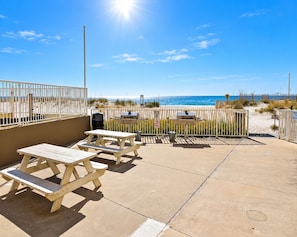 A beachside patio with picnic tables and barbecue grills, overlooking the ocean. - Time to get… 🎶 Knee deep in the water somewhere! 🎶 on island time! (Gulf Shores)
