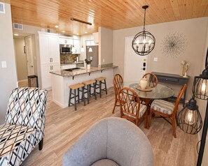 A modern kitchen with white cabinets, a central island with stools, and a dining area with a glass table and wicker chairs.