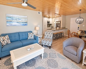A living room with a blue sofa, patterned armchairs, a white coffee table, and a patterned rug. - Time to get… 🎶 Knee deep in the water somewhere! 🎶 on island time! (Gulf Shores)