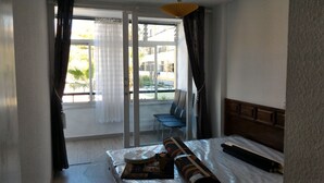 Una habitación de hotel con cama, una silla, un ventanal con cortinas y vistas al exterior.