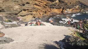 Una playa rocosa con gente tomando el sol y nadando, rodeada de acantilados.