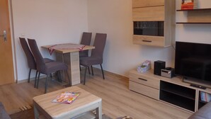 A compact living space with a dining table, two chairs, a small TV, and a cabinet with shelves. - Cable car, lift, slopes, ski schools are within walking distance. Family friendly (Kurort Oberwiesenthal)