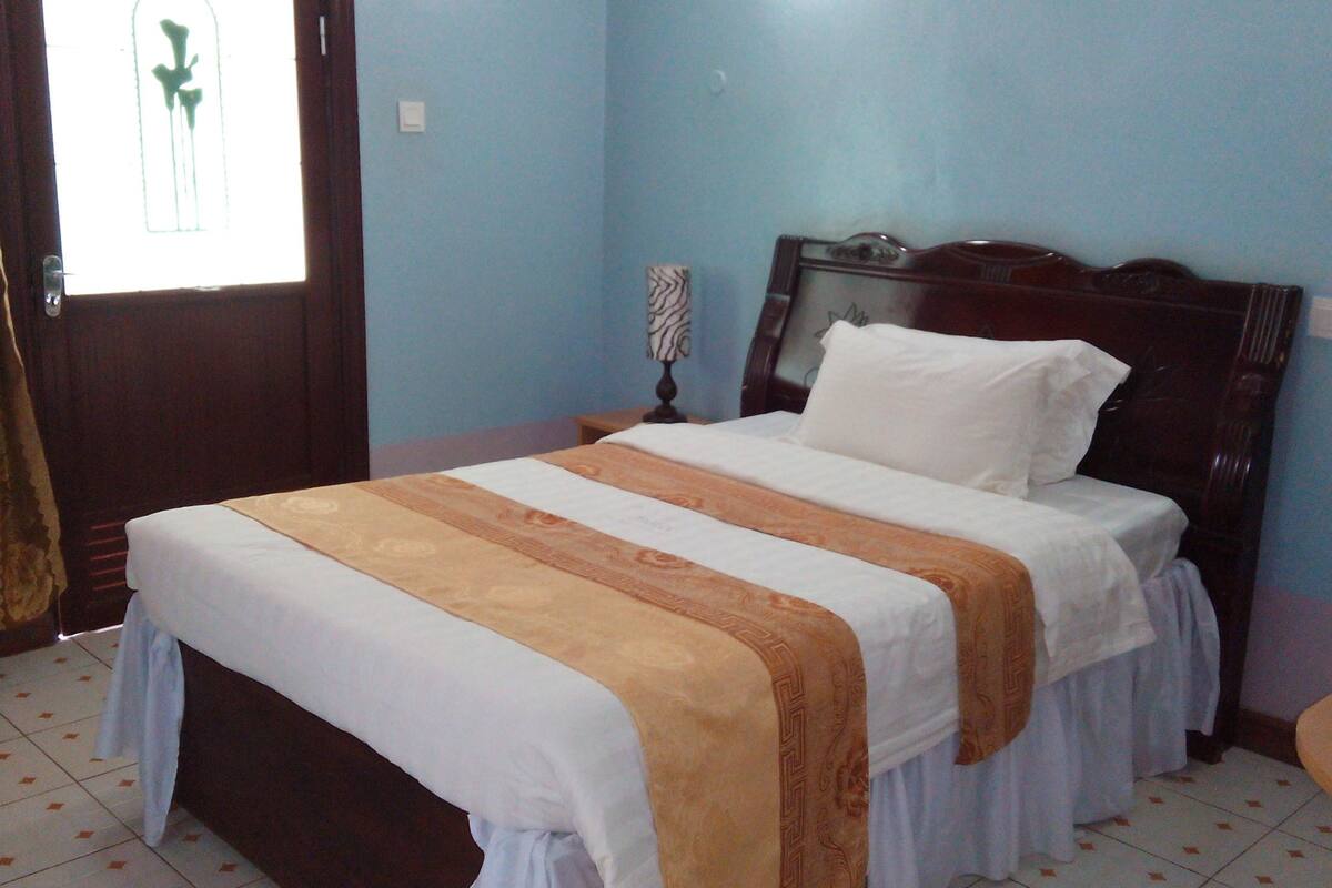 A bedroom with a bed, a nightstand, a lamp, and a window with curtains.