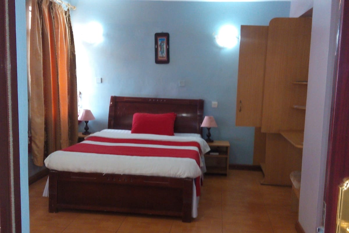 A bedroom with a wooden bed, a red pillow, two bedside lamps, a nightstand, and a wooden wardrobe.