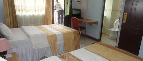 A hotel room with two beds, a desk with a computer, a chair, and a toilet.