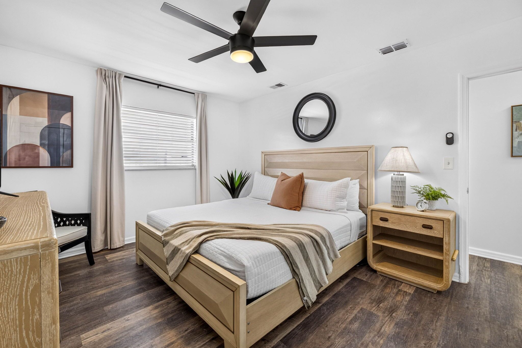 Een slaapkamer met een bed, nachtkastje, lamp en een plafondventilator.