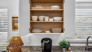 Een keuken met een inbouwkastplank met verschillende kommen en borden, een koffiezetapparaat, een bloempot en een rieten lamp.