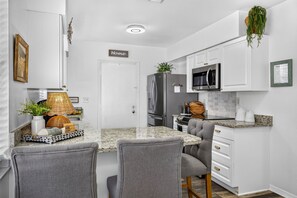 Une cuisine moderne avec des meubles blancs, un plan de travail en granit, une cuisinière à deux brûleurs, un réfrigérateur et un four à micro-ondes.