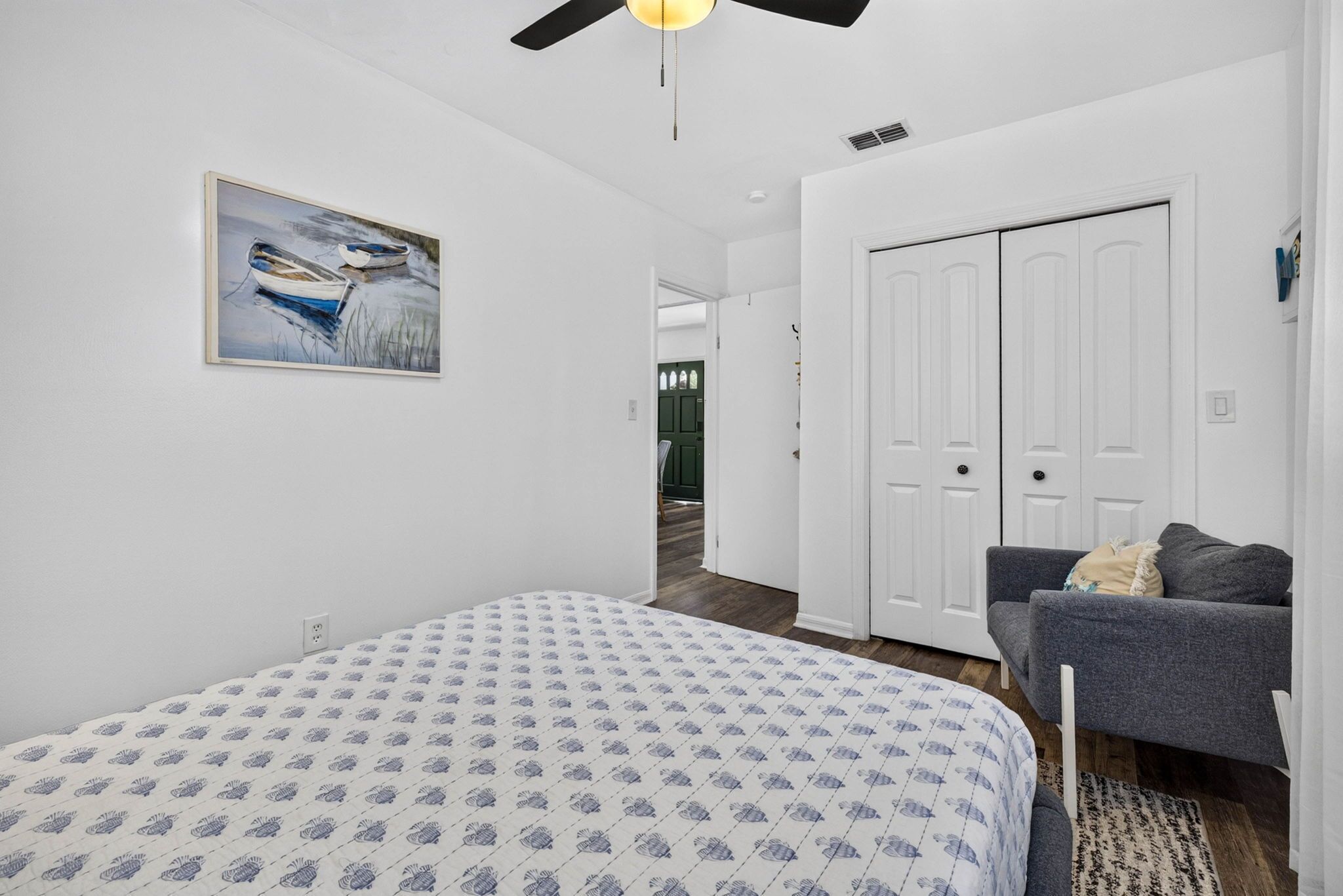 A bedroom with a bed, a gray sofa, a white door, and a painting on the wall.