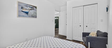 A bedroom with a bed, a gray sofa, a white door, and a painting on the wall.