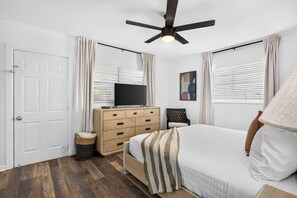 Une chambre à coucher comprenant un lit, une commode, un téléviseur et un ventilateur de plafond.