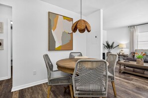 Ein Essbereich mit einem runden Holztisch, vier Korbstühlen, einer hängenden Leuchte und einem modernen abstrakten Gemälde an der Wand.