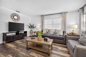 A modern living room with a flat-screen TV, a sofa, a coffee table with decorative items, and a television cabinet.