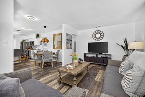 A modern living room with a dining area, a flat-screen TV, and a sofa.