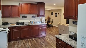 A kitchen with wooden cabinets, a granite countertop, a stove, a refrigerator, and a dining area with a table and chairs. - Maggie Valley Mountain View Suite & Spa (Maggie Valley)