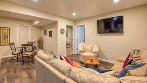 A living room with a beige sofa, a dining table with chairs, a TV mounted on the wall, and a wooden floor. - Maggie Valley Mountain View Suite & Spa (Maggie Valley)