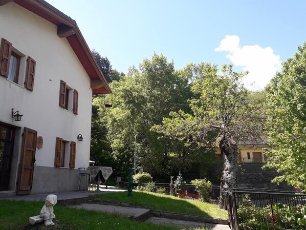 A white building with brown shutters, a small garden with a statue, and a tree with a stone staircase. - B&b La Tana Dei Ricci (Sestola)