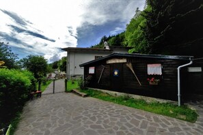 A stone pathway leading to a rustic wooden building with a signboard, surrounded by greenery and a clear sky. - B&b La Tana Dei Ricci (Sestola)