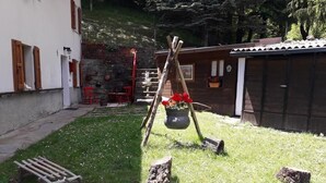 Un espacio exterior rústico con una mecedora de madera, una maceta colgante y un banco de madera.