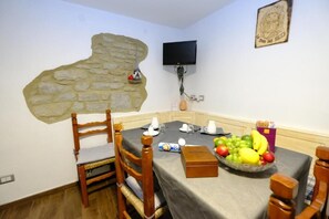 A dining area with a stone wall mural, a television mounted on the wall, and a table set with a fruit bowl and a box of tissues. - B&b La Tana Dei Ricci (Sestola)