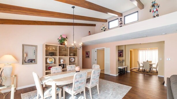 A spacious dining area with a wooden table and chairs, a chandelier, and a bookshelf filled with decorative items.