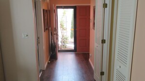 A hallway with hardwood floors, a white door at the end, and a view of the outside.