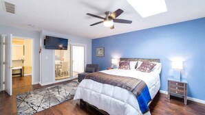 A bedroom with a bed, a ceiling fan, a TV, and a nightstand with a lamp.