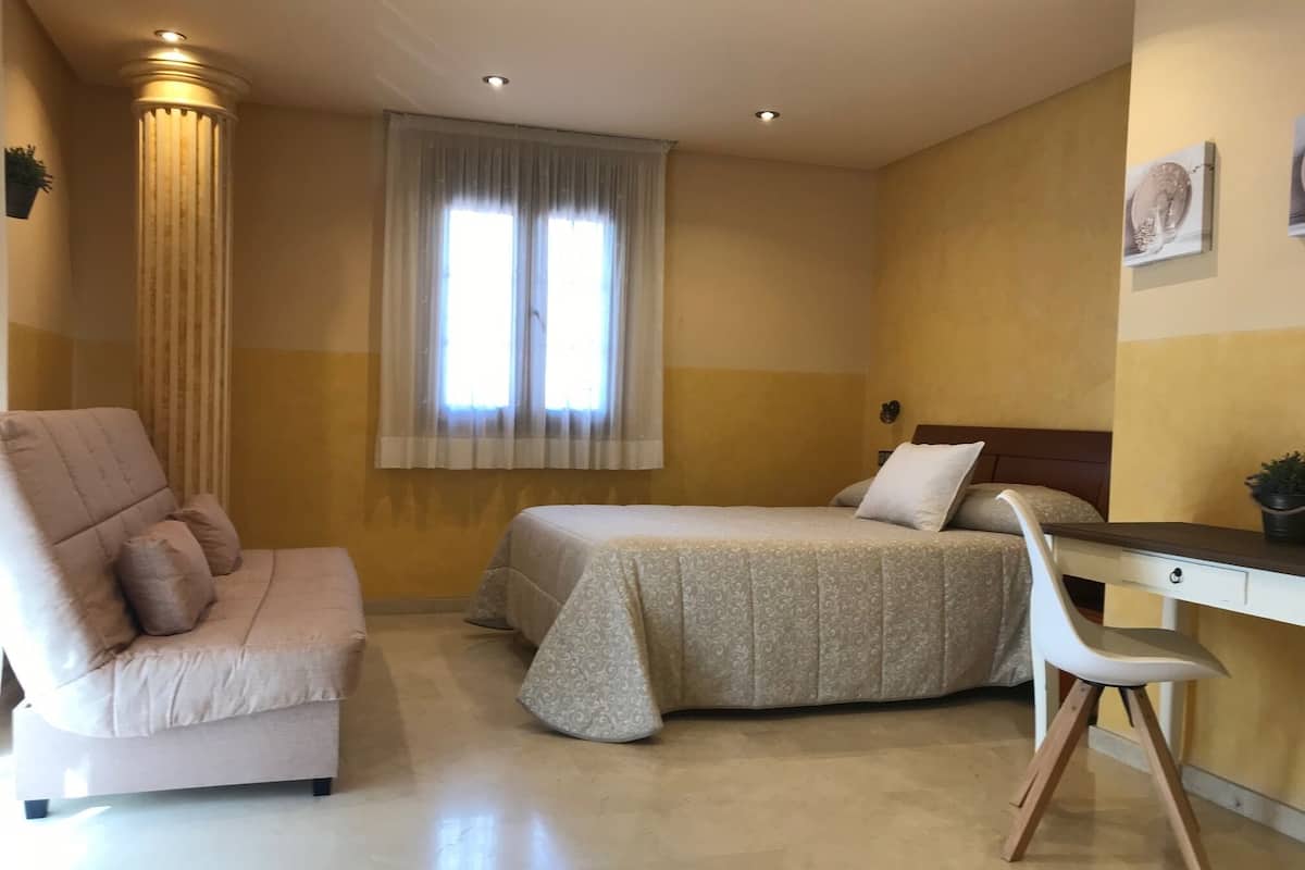 A bedroom with a bed, a desk, a chair, and a couch.