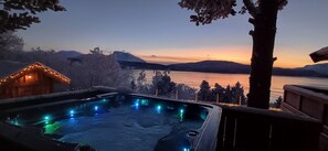 A hot tub with a view of a lake and mountains at dusk.