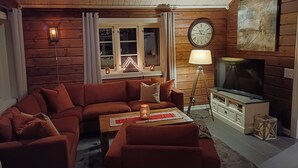 Une chambre confortable, aménagée dans le style d’un chalet, avec un canapé d’angle, un téléviseur et une lampe.