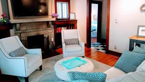 A living room with a fireplace, two white armchairs, a round ottoman, and a sofa with patterned cushions. - 2 blocks to North Chattanooga revitalized riverfront restaurants and bars. (Chattanooga)