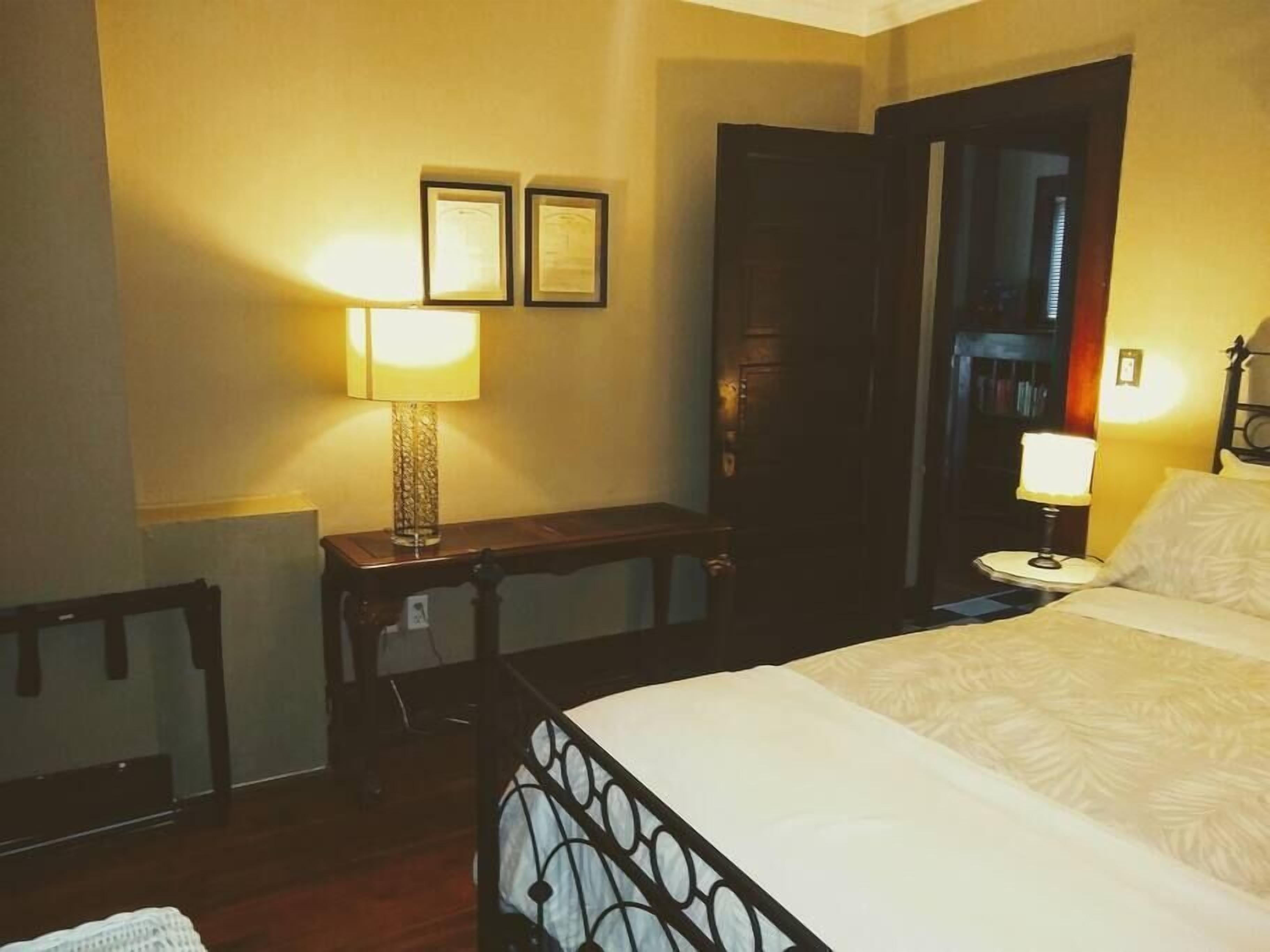 Camera d'albergo con un letto, due lampade ai comodini, un tavolino, una sedia e due quadri appesi al muro.