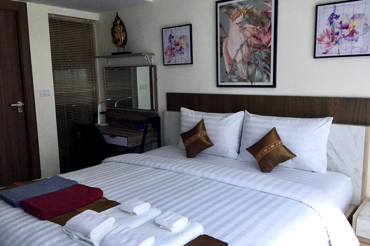 A hotel room with a large bed, a desk, and a mirror. There are towels on the bed and a painting on the wall.