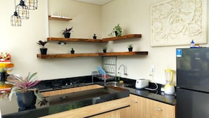 Een moderne keuken met houten planken waarop potplanten staan, een zwarte koelkast, een spoelbak met een afdruiprek en een gasfornuis.