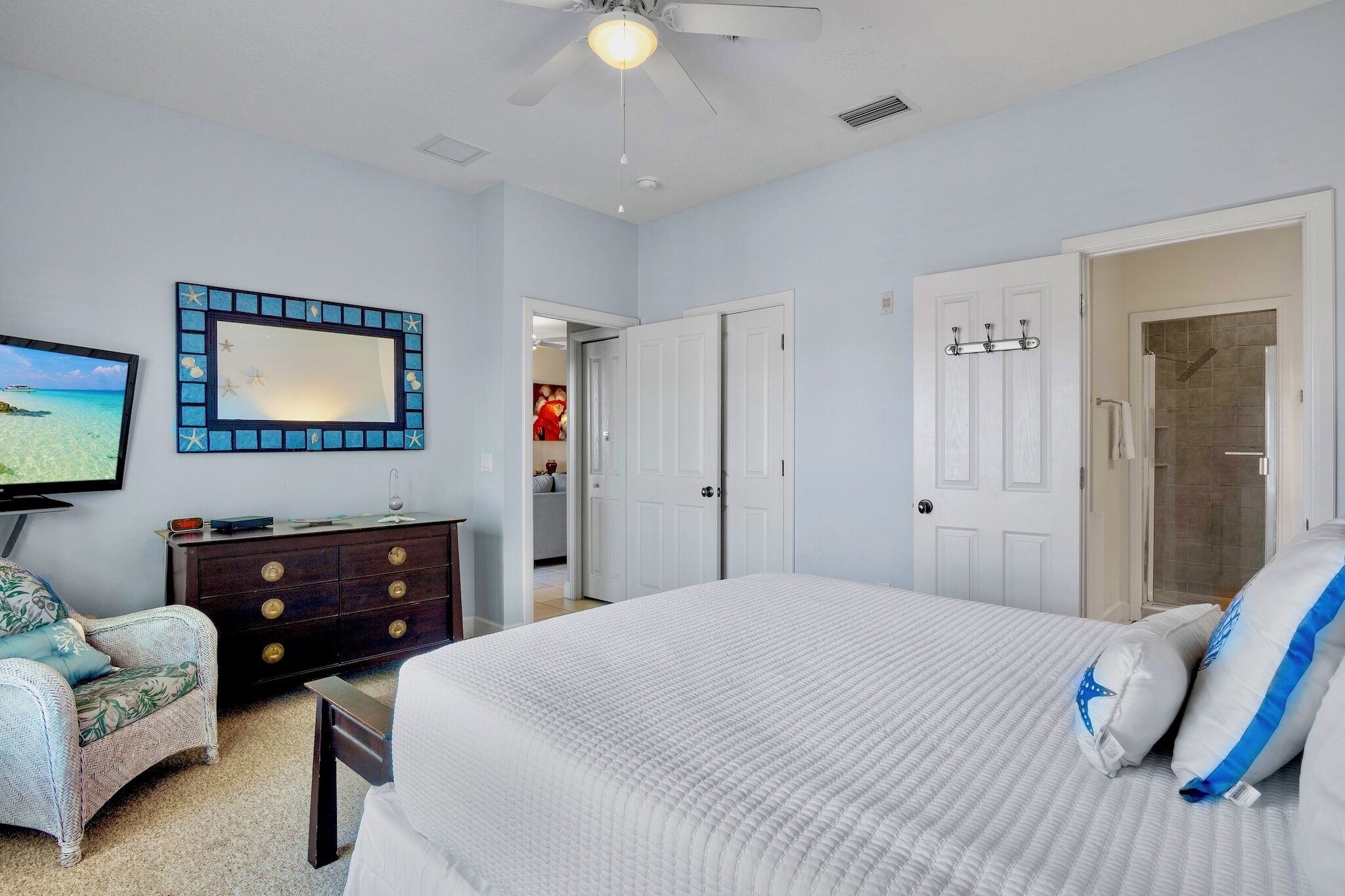 A bedroom with a bed, a dresser, a chair, a mirror, and a door leading to a bathroom.