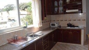 Cocina con lavaplatos, microondas y estufa. Se ve un ventanal con cortinas y vistas a zonas verdes.